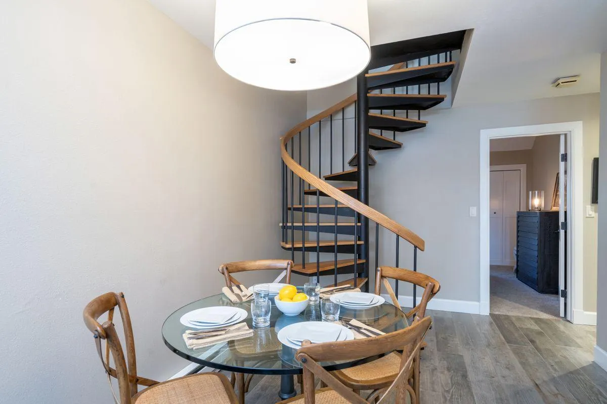 A cozy dining area anchored by a dining table under a stylish light fixture, with the spiral staircase visible in the background. The setup is perfect for intimate meals, social gatherings, and shared stories, echoing the warmth and connection described in the section.