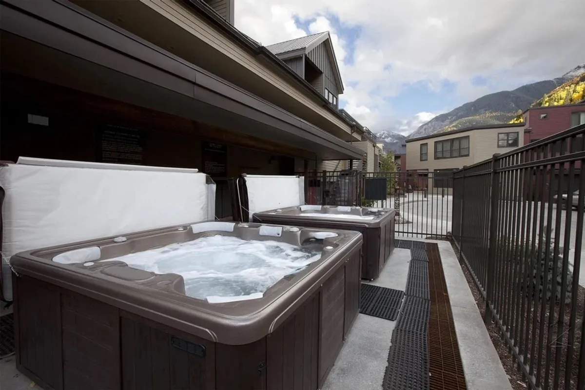 This image features inviting outdoor hot tubs set within a fenced area, surrounded by stunning mountain views. The steam rising from the bubbling water hints at relaxation and social gatherings against a picturesque alpine backdrop.