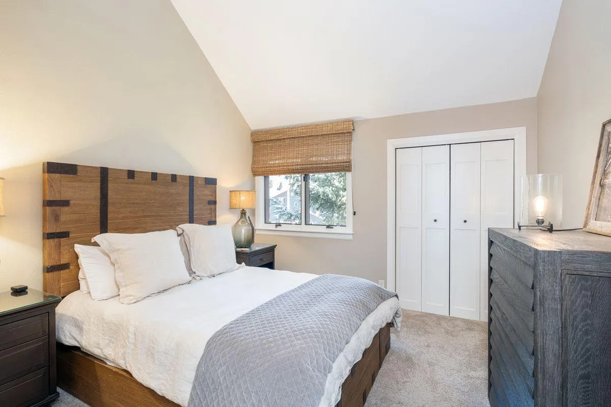 A tranquil second bedroom with a comfortable bed, bedside nightstand, window letting in morning light, and a dresser. The neutral tones and simple decor create a peaceful environment ideal for guests or family members.