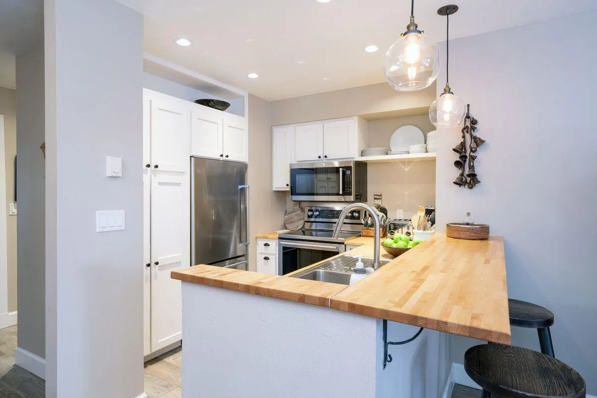 A welcoming kitchen interior with a spacious island, sleek stainless steel appliances, and warm pendant lighting, suggesting a spot for gathering, prepping meals, or entertaining. The wooden countertop and modern design blend comfort with utility.