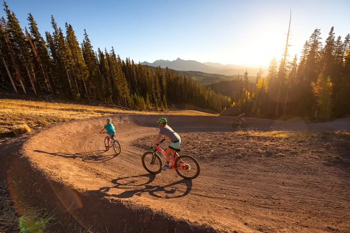 An exciting exterior shot featuring mountain bikers riding along a curved trail surrounded by lush natural scenery. The trail winds through trees and open spaces, evoking a sense of adventure and active exploration in the great outdoors.