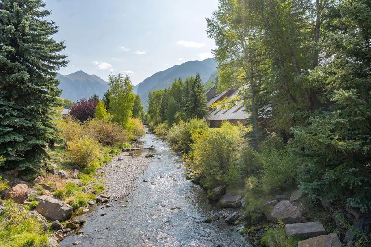 A sweeping view along a scenic pathway beside a flowing river, lush greenery, and mountain backdrop. The area is alive with possibilities for hiking, picnicking, and enjoying serene nature during the warmer months.