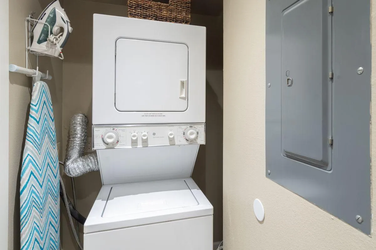 The interior laundry area is equipped with a stacked washer and dryer, an iron and ironing board, and a storage basket. The organized space underscores practicality and home-like convenience for longer stays or families.