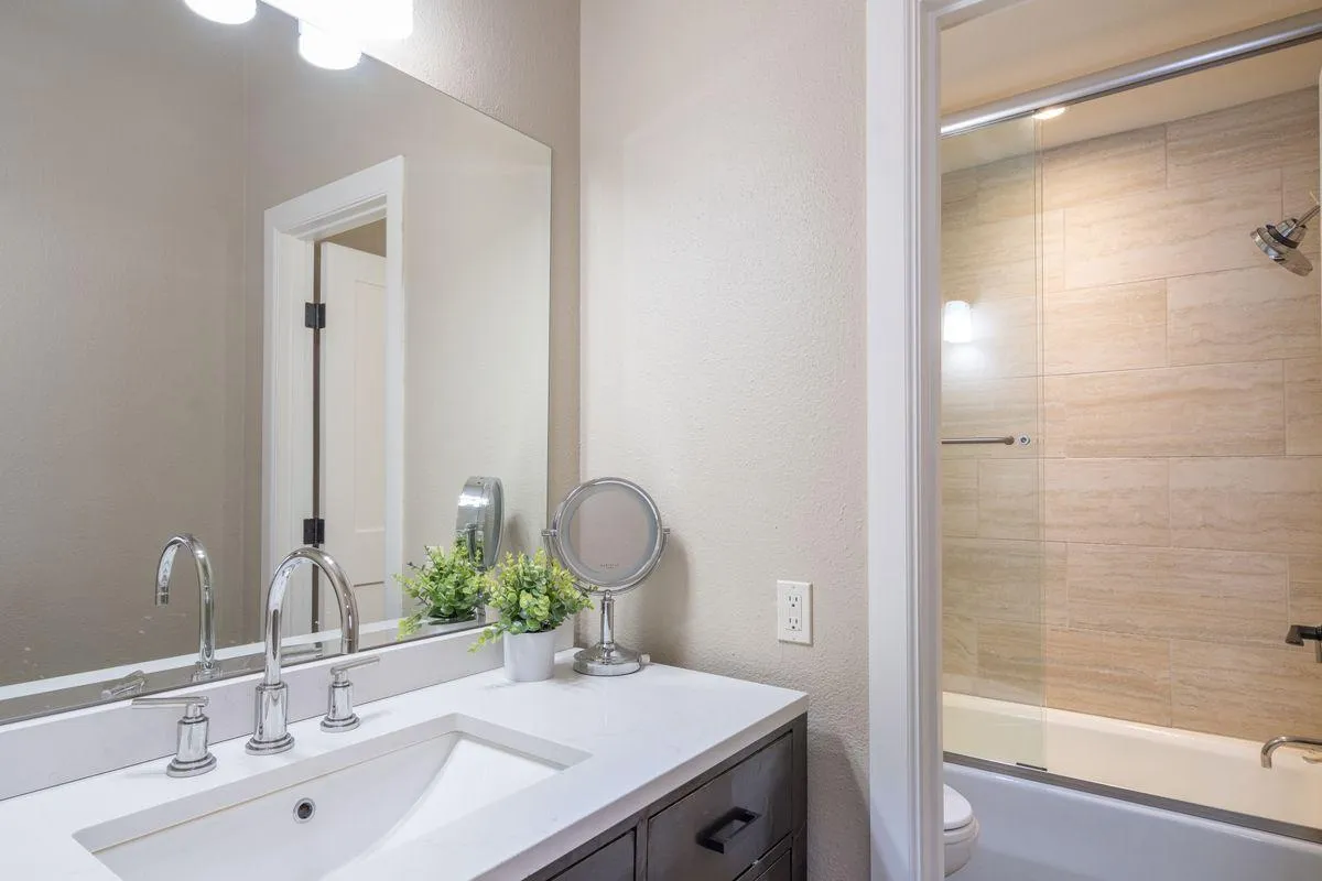 A modern, inviting bathroom featuring a stylish vanity with sink, a mirror, a shower area, and green plants for a touch of freshness. The layout is bright and well-appointed, perfect for morning routines or relaxing after a day outdoors.