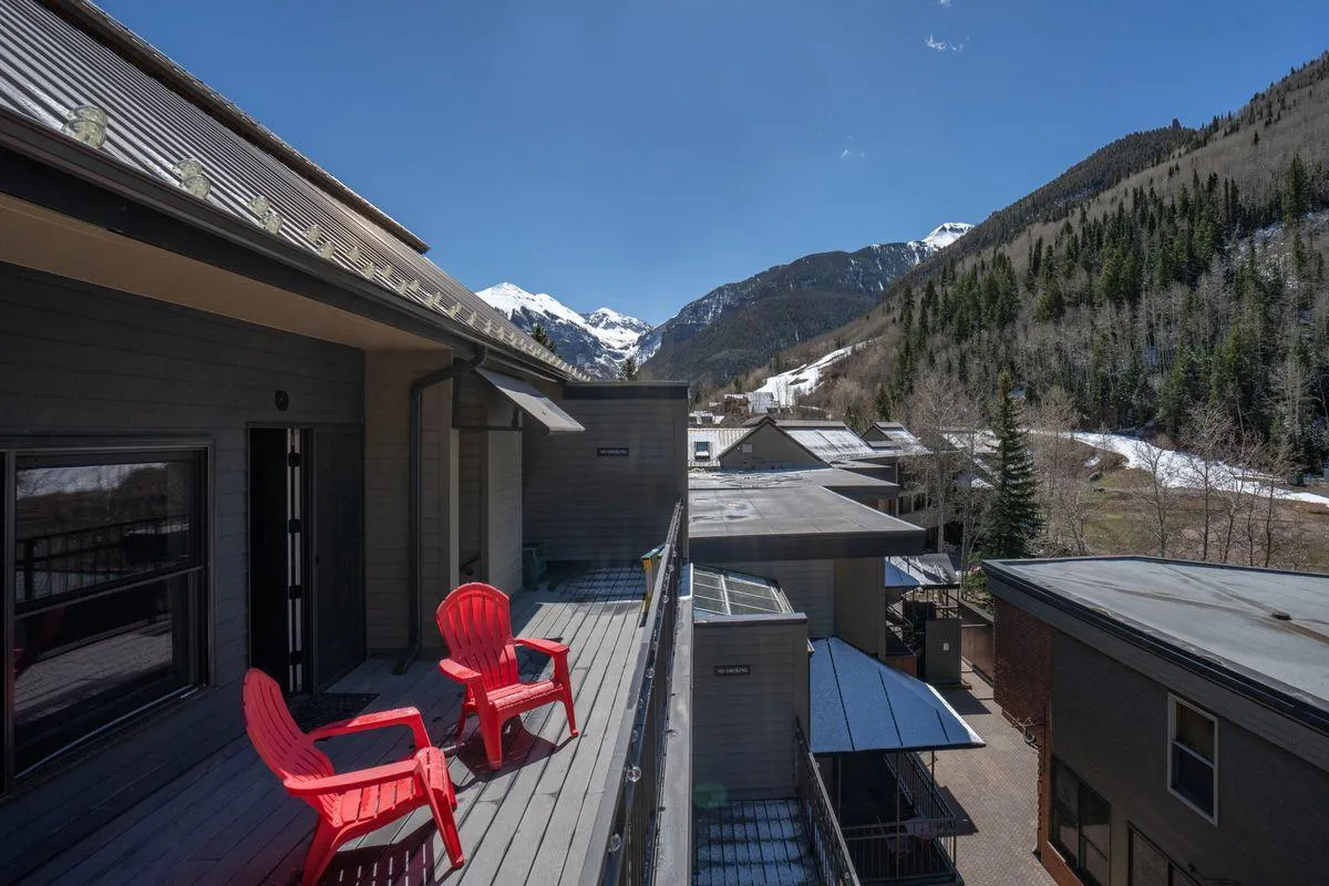 A wooden deck with red Adirondack chairs facing a magnificent mountain view. The outdoor space is serene and inviting, ideal for enjoying morning coffee or evening drinks while soaking up the alpine scenery.
