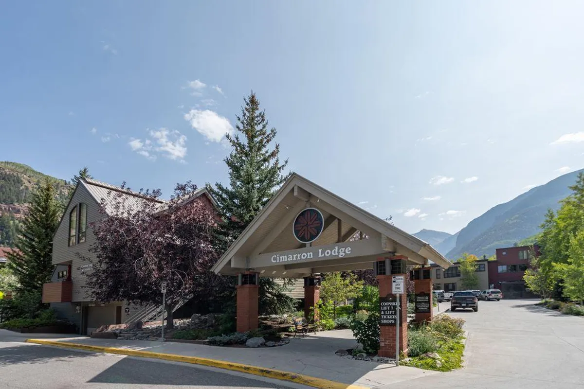 The welcoming entrance of Cimarron Lodge, featuring the building’s sign, an inviting awning, and mature trees framing the exterior. The scene feels approachable and sets the tone for a comfortable stay.